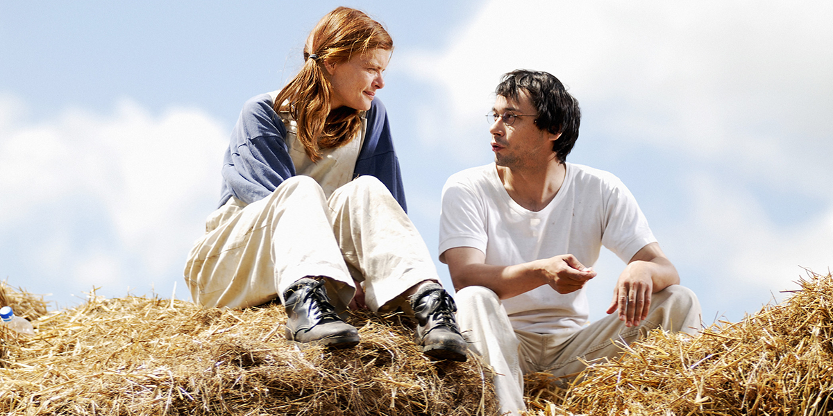 Photo of man and woman talking while seated on bail of hay